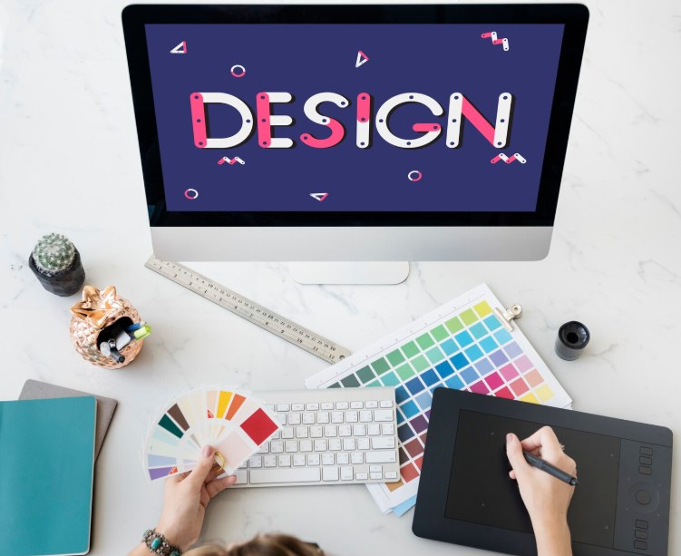 A designer's desk with a screen showing the word DESIGN, colour swatches and a drawing tablet