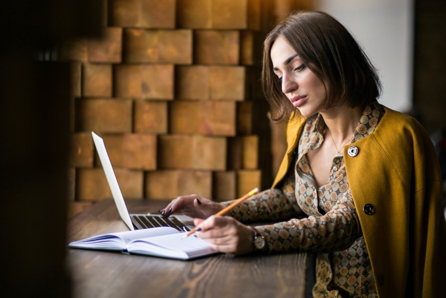 A writer working on her laptop and notes at a wooden desk
